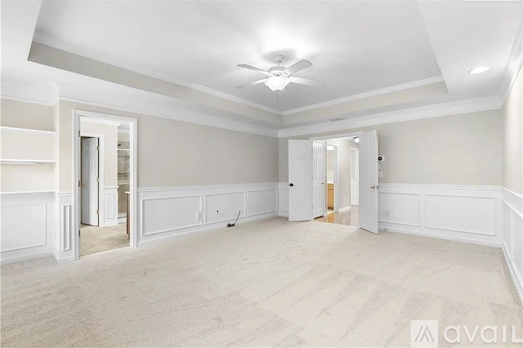 A spacious room with a ceiling fan and light, carpeted flooring, and white walls with paneling.