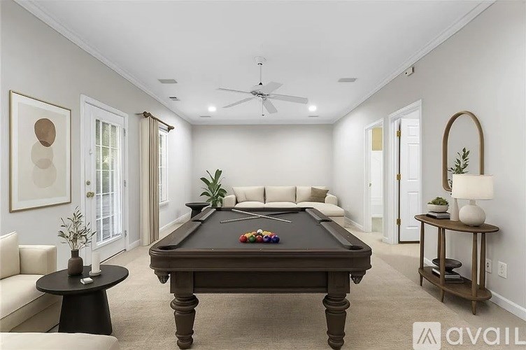 A pool table is in the middle of a room with a fan and a plant.