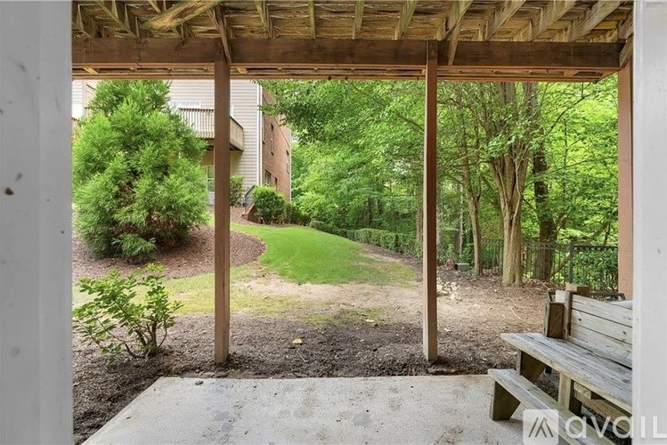 A wooden pergola overlooks a backyard with a lawn and trees.