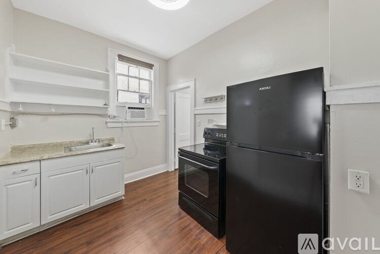 A black fridge in a kitchen with white cabinets and a marble countertop.