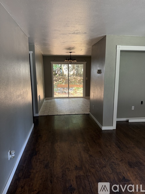 A room with wood flooring and a doorway leading to a backyard.