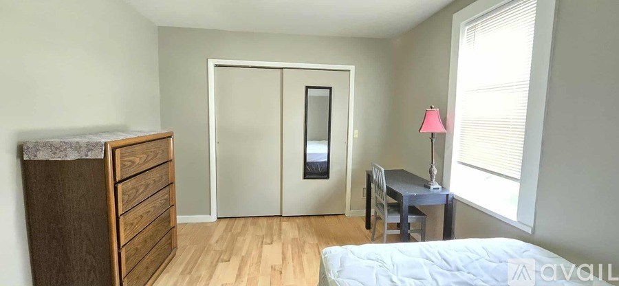 A bedroom with a bed, dresser, desk, and a window with blinds.