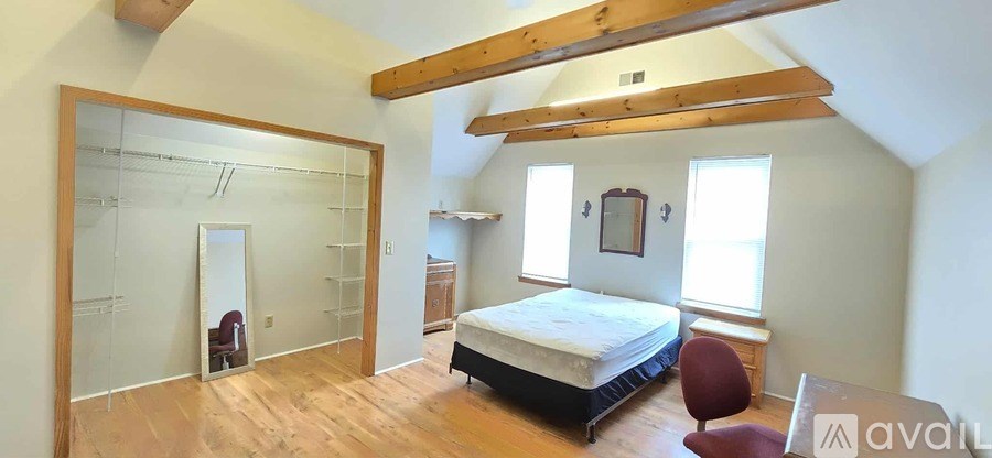 A bedroom with a bed, a chair, and a mirror.