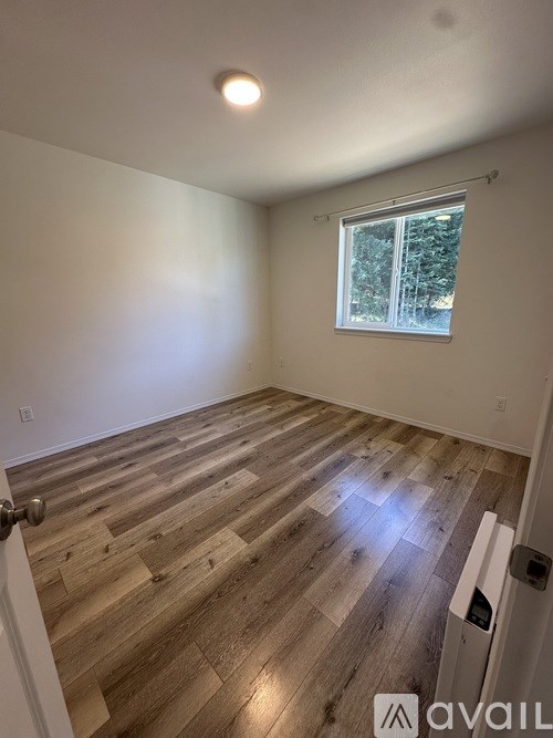 A room with wooden flooring and a window showing trees outside.