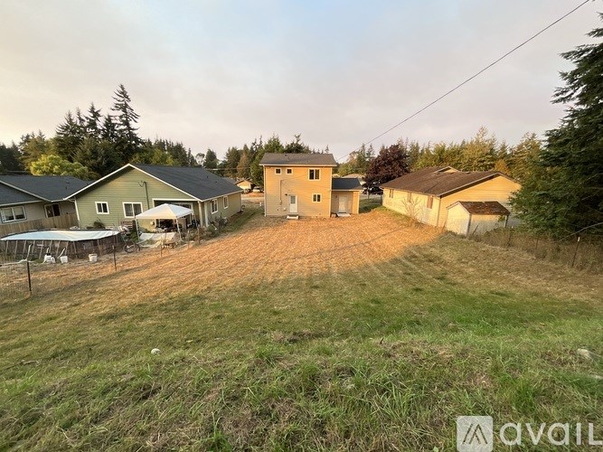 A dirt road leads to a small house with a fence and a tree in the background.