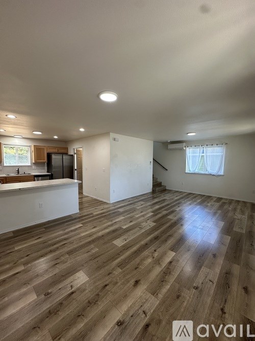 A spacious room with wooden flooring and a window with white curtains.