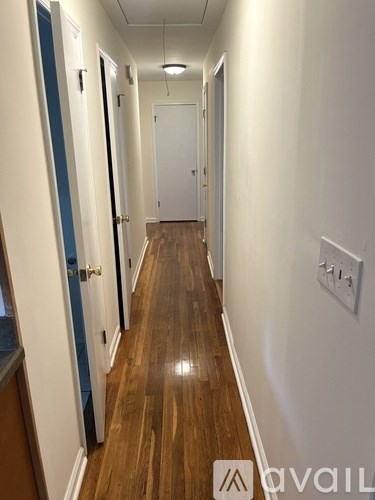 A long hallway with doors on both sides and a light switch on the wall.