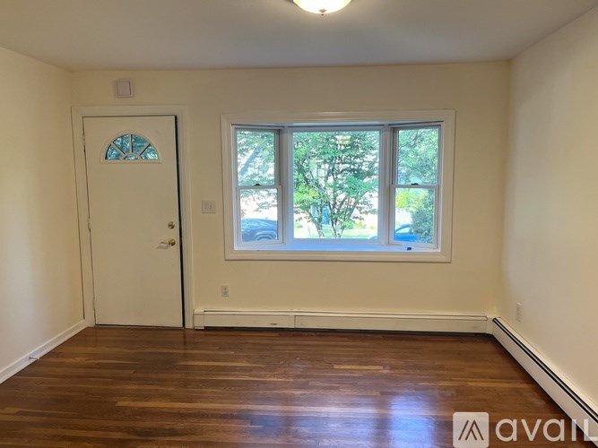 A room with a white door and a window with a view of trees.