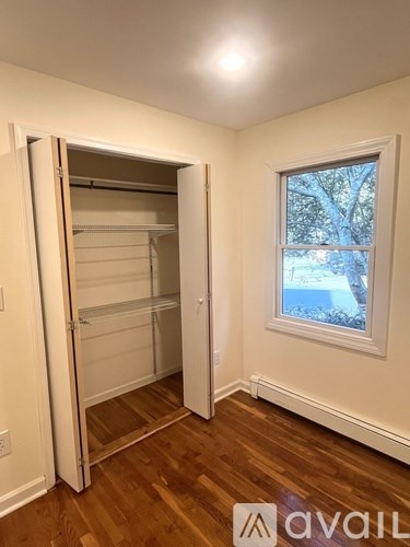 A room with a wooden floor and a white wall with a window and a wooden door.