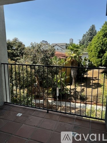 A balcony with a black railing and a view of a garden and buildings.