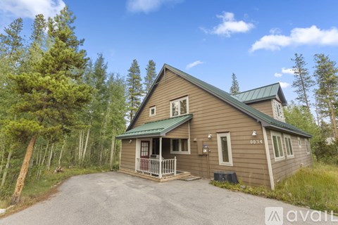 A house with a green roof is surrounded by trees and has a driveway in front.