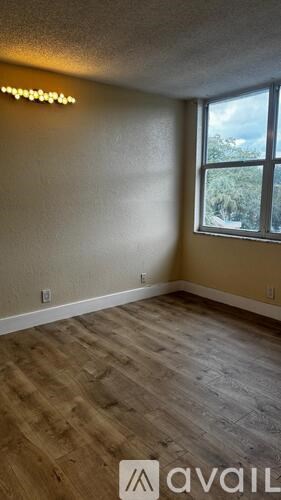 A room with wooden flooring and a window showing trees outside.