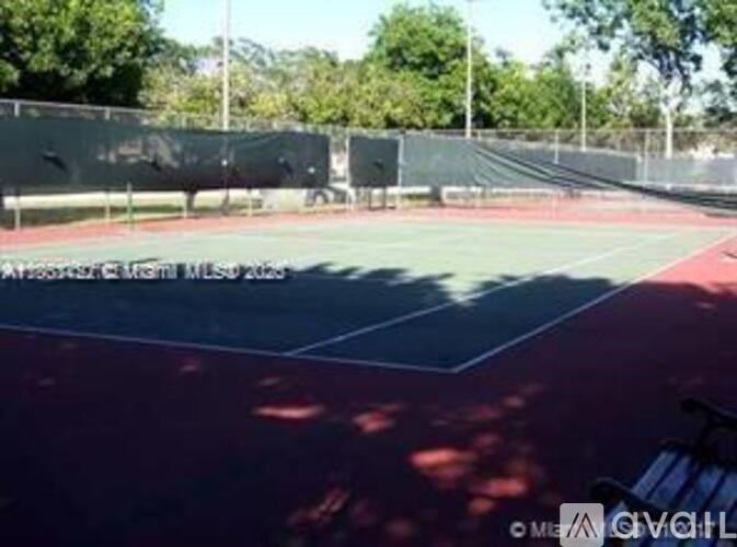 A tennis court with a fence and trees in the background.