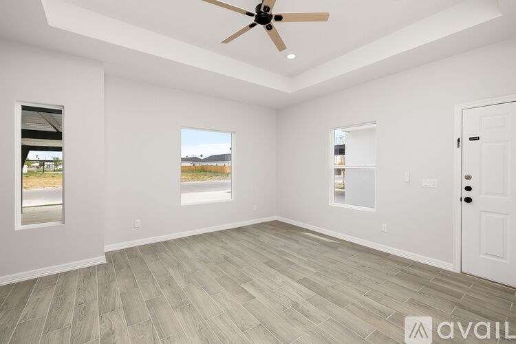 A spacious room with a ceiling fan and lighting, featuring a wooden floor and white walls.