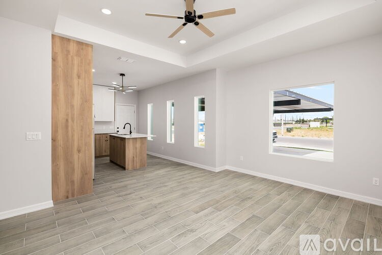 A spacious room with a ceiling fan and a kitchen area with a sink and cabinets.