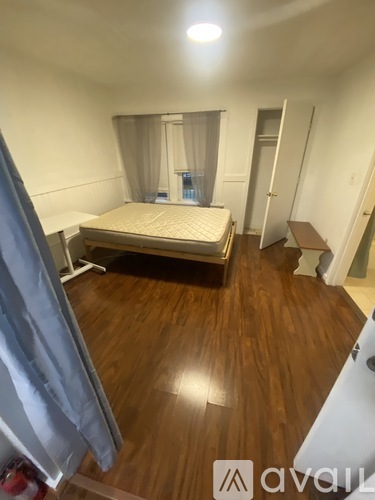 A bedroom with a bed, wooden floor, and a window with curtains.