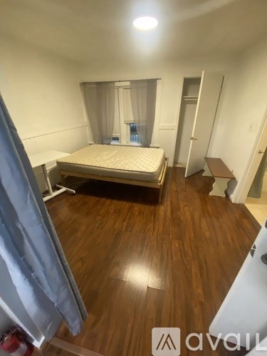 A bedroom with a bed, wooden floor, and a window with curtains.
