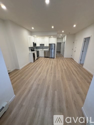 A spacious room with wooden flooring and a kitchen area in the background.