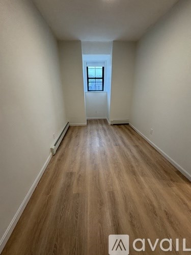 A long hallway with wooden floors and a window at the end.