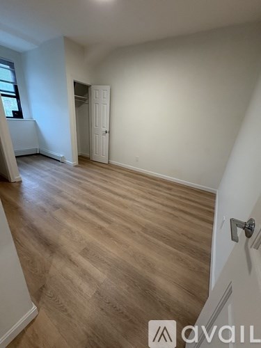 A room with wooden flooring and white walls, with a door on the right side.