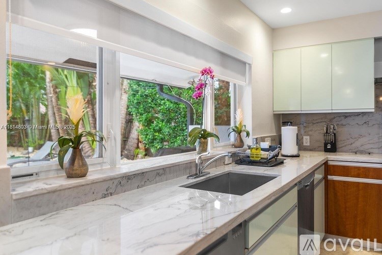 A kitchen with a marble countertop and a window overlooking a lush garden.