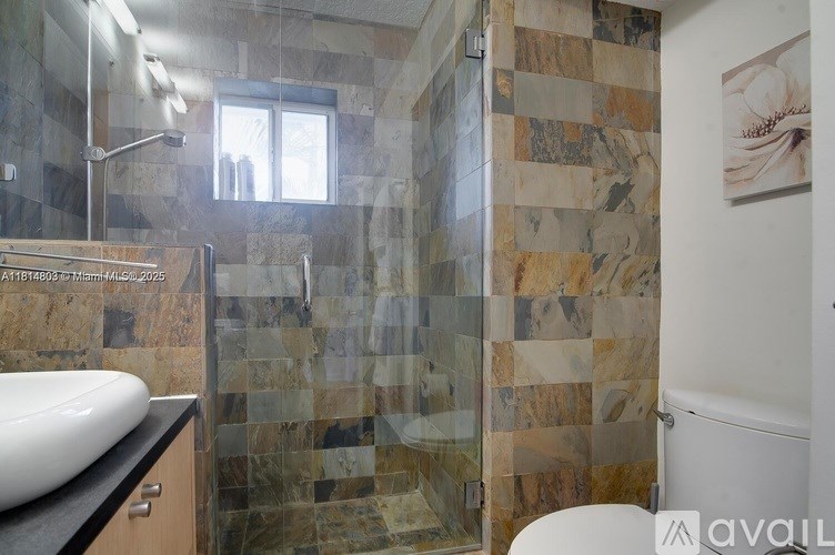 A bathroom with a marble tile shower and a white sink.