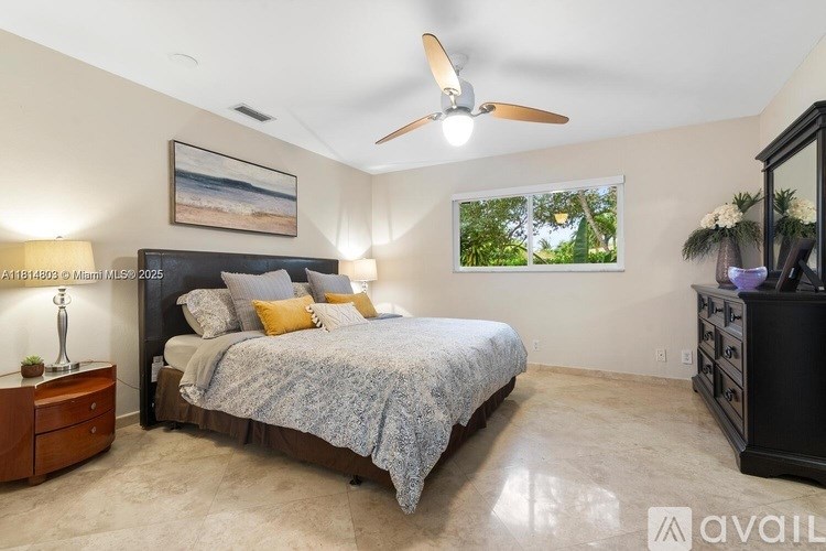 A bedroom with a large bed, a ceiling fan, and a painting on the wall.