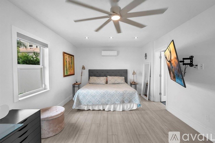 A bedroom with a bed, a ceiling fan, and a painting on the wall.