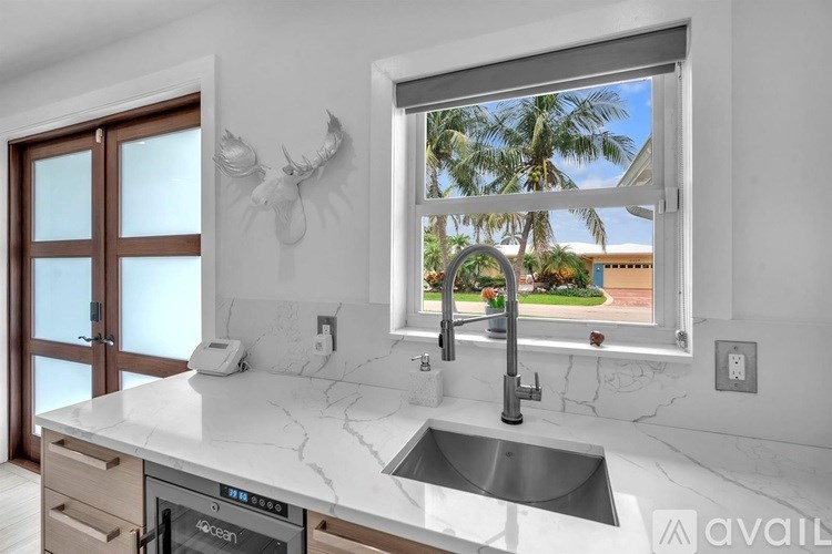 A modern kitchen with a marble countertop and a window overlooking a palm tree-lined street.