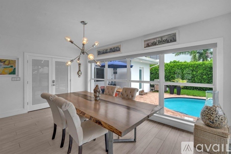 A dining room with a wooden table and chairs, a chandelier, and a view of a pool and greenery outside.