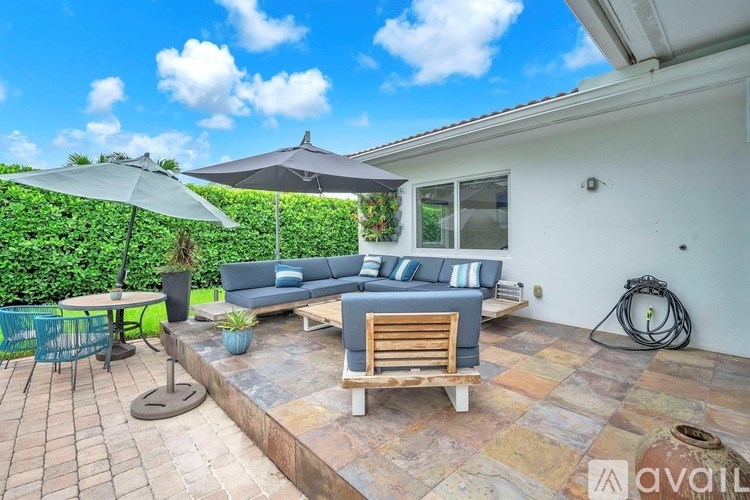 A patio with a sofa, chairs, and a table with a green hedge in the background.