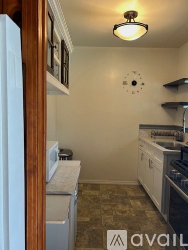 A kitchen with a clock on the wall and a refrigerator on the left.