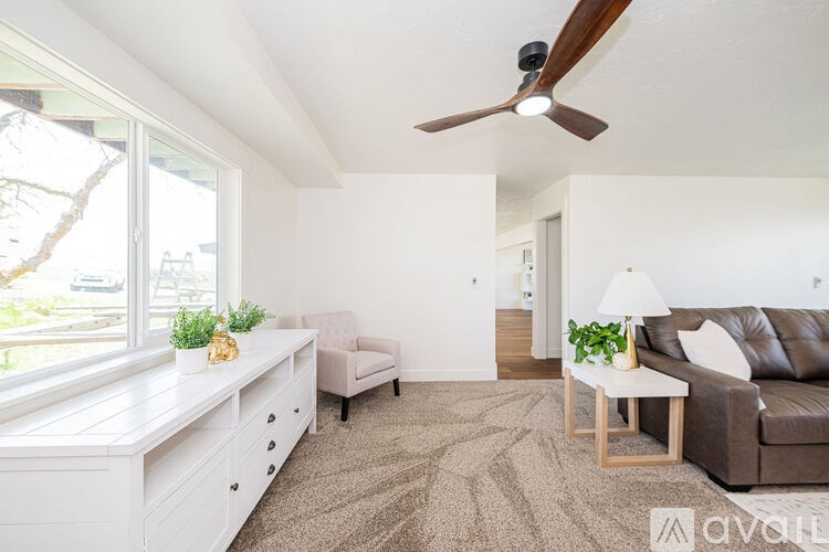 A living room with a brown couch, a white chair, and a white dresser with a window.