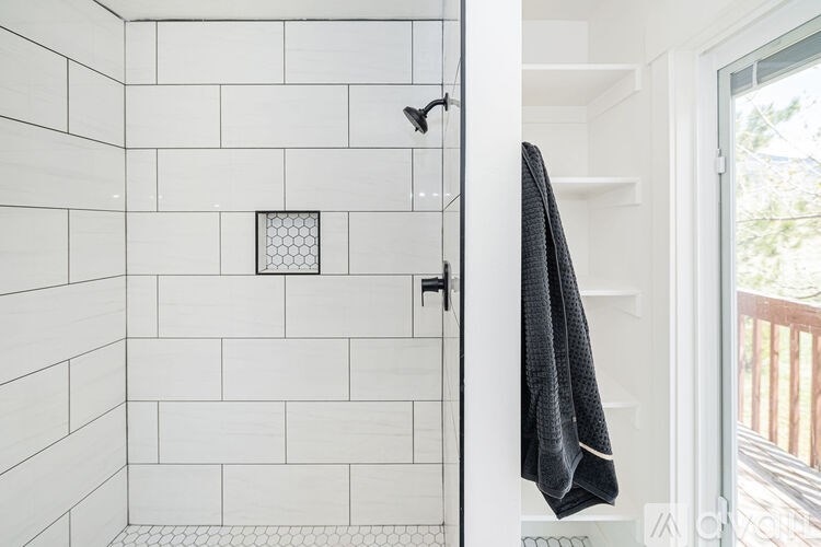 A black towel hangs on a white door in a white tiled bathroom.
