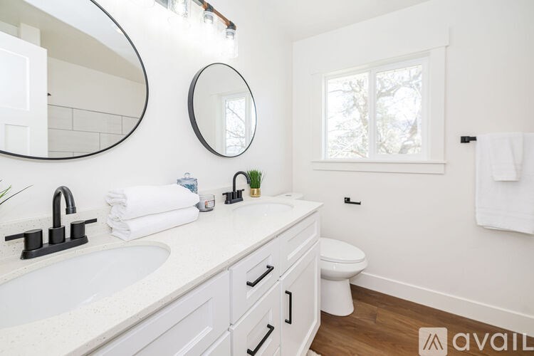 A bathroom with a white sink, toilet, and a round mirror above the sink.