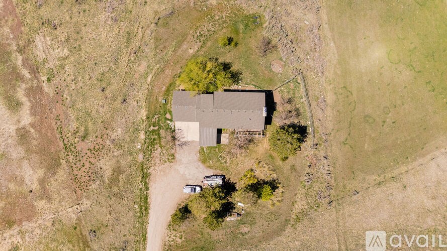A house with a grey roof is surrounded by a dirt road and greenery.