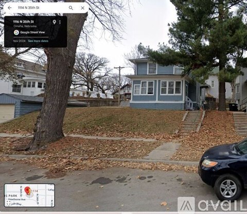 A street view of a residential area with a blue house and a tree in the foreground.