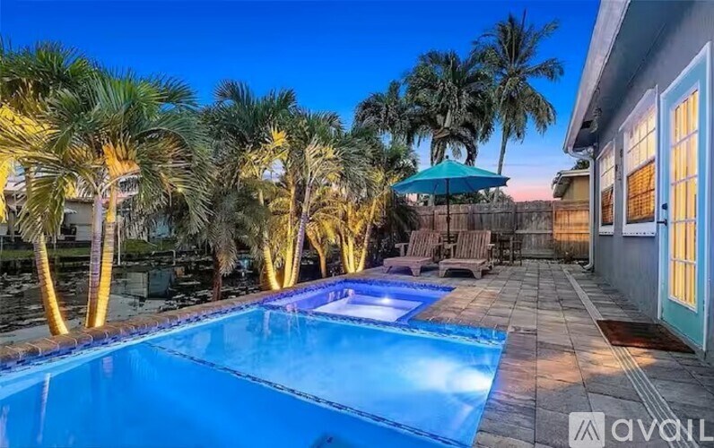 A pool surrounded by palm trees and a house with a blue umbrella.