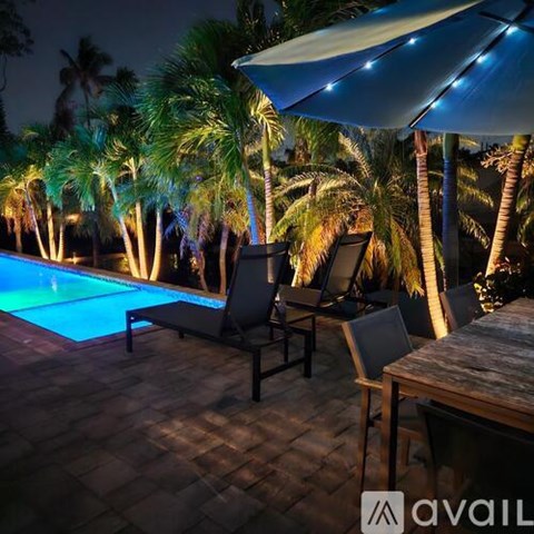 A pool surrounded by palm trees and a house with a blue umbrella.