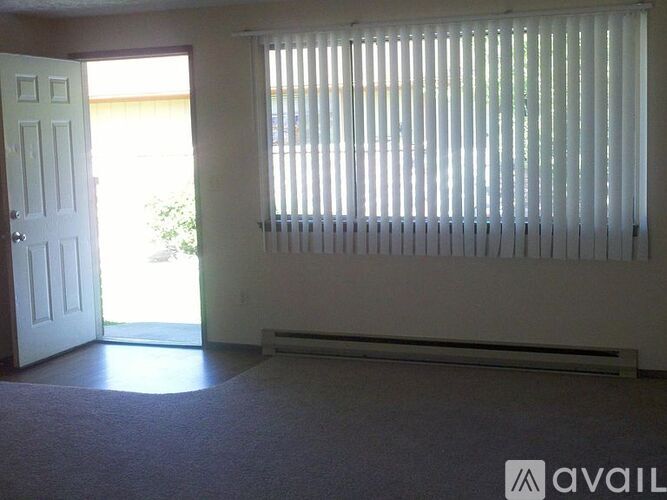 A room with a carpeted floor, a door, and a window with blinds.