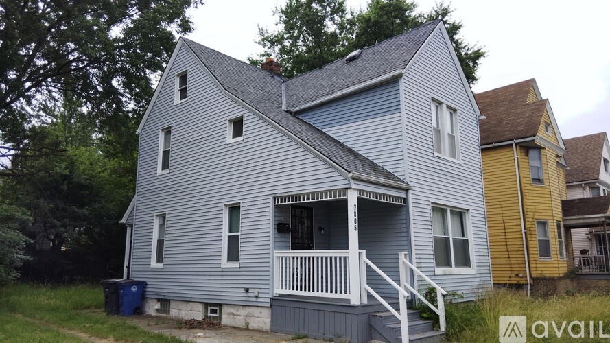 A blue house with a porch and a trash can in front.