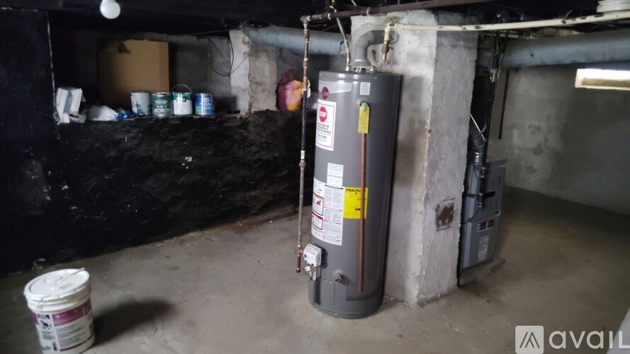 A grey water heater with a yellow label is in a basement.