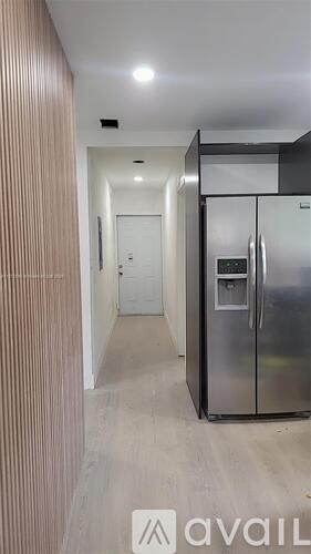 A kitchen with a stainless steel refrigerator and wooden paneling on the wall.