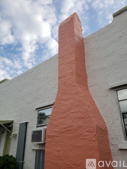 A tall, red, chimney-like structure stands in front of a white building.