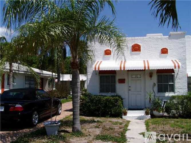 A black car is parked in front of a white house with a palm tree.