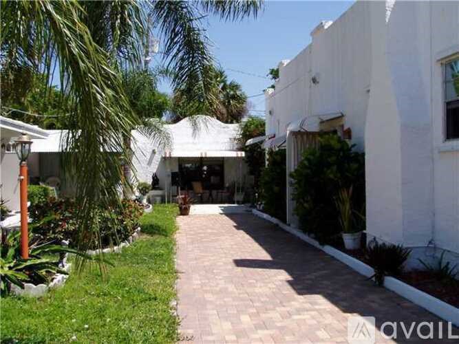 A white building with a white awning is surrounded by green plants.