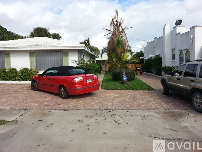 A red car is parked in front of a white house.