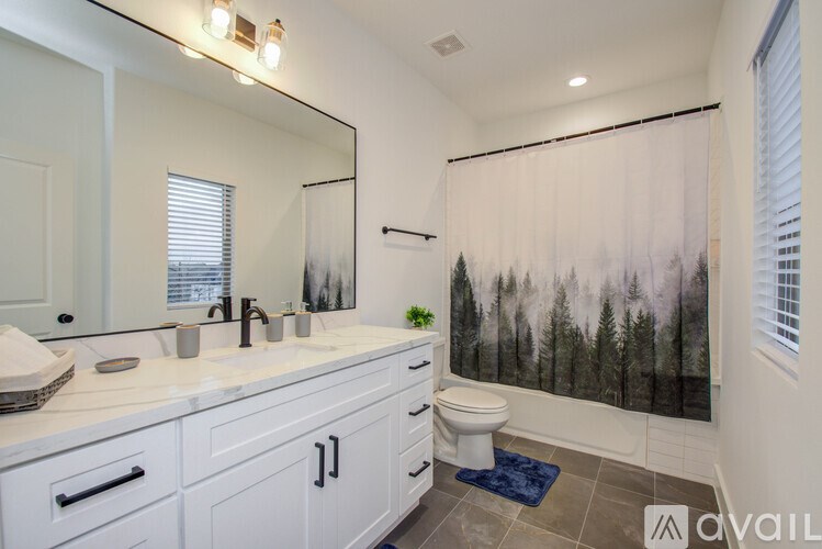 A bathroom with a white counter top and a forest wallpapered shower.