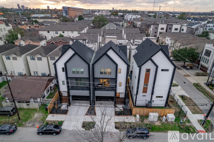 A modern house with a black roof and white walls is surrounded by other houses.