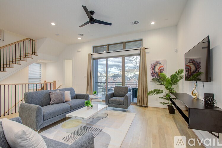 A living room with a grey couch, a white coffee table, a grey armchair, a black TV and a plant.